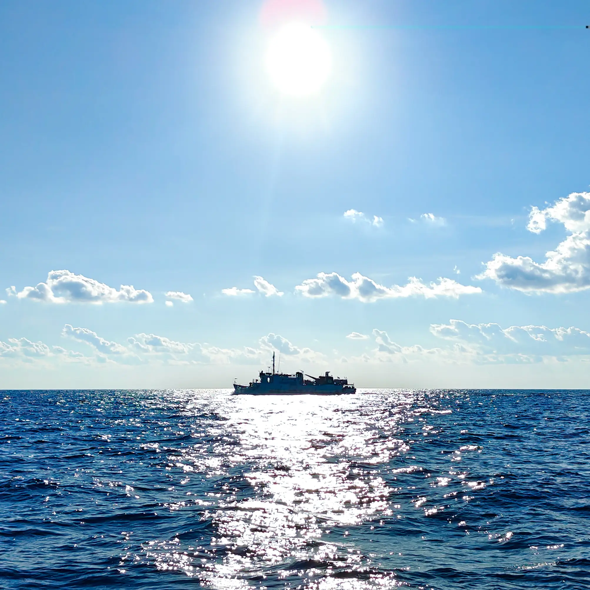 A small boat silhouetted on open water, backlit by a low, bright sun with its light scattered across the waves.